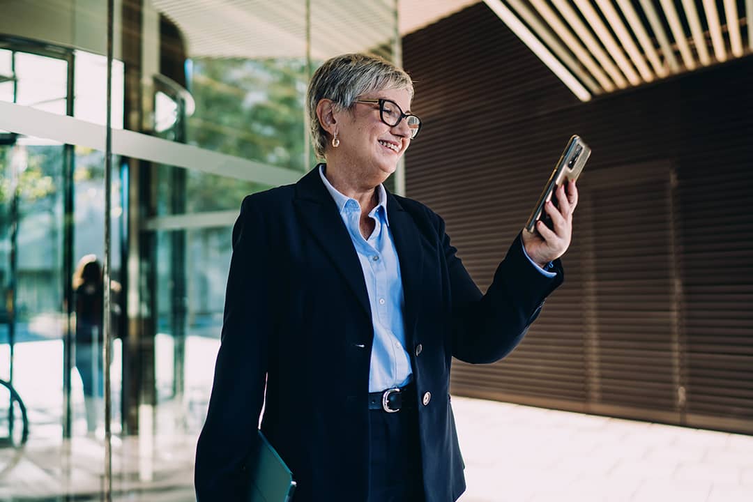 A senior businesswoman smiling at smartphone screen.